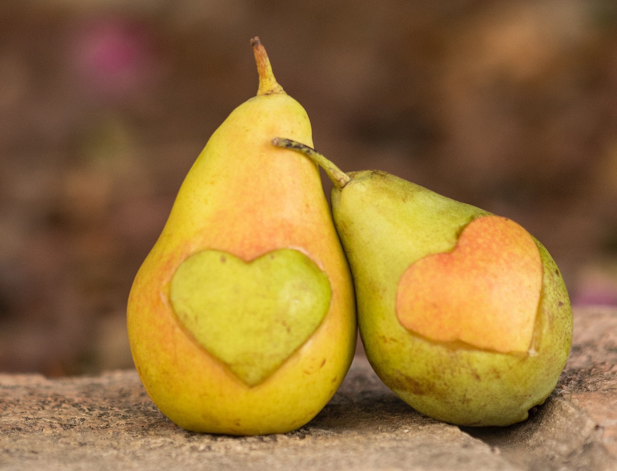An artwork of two pears with each having a heart shape removed from the skin and placed on the other pear, representing connectivity through the heart.