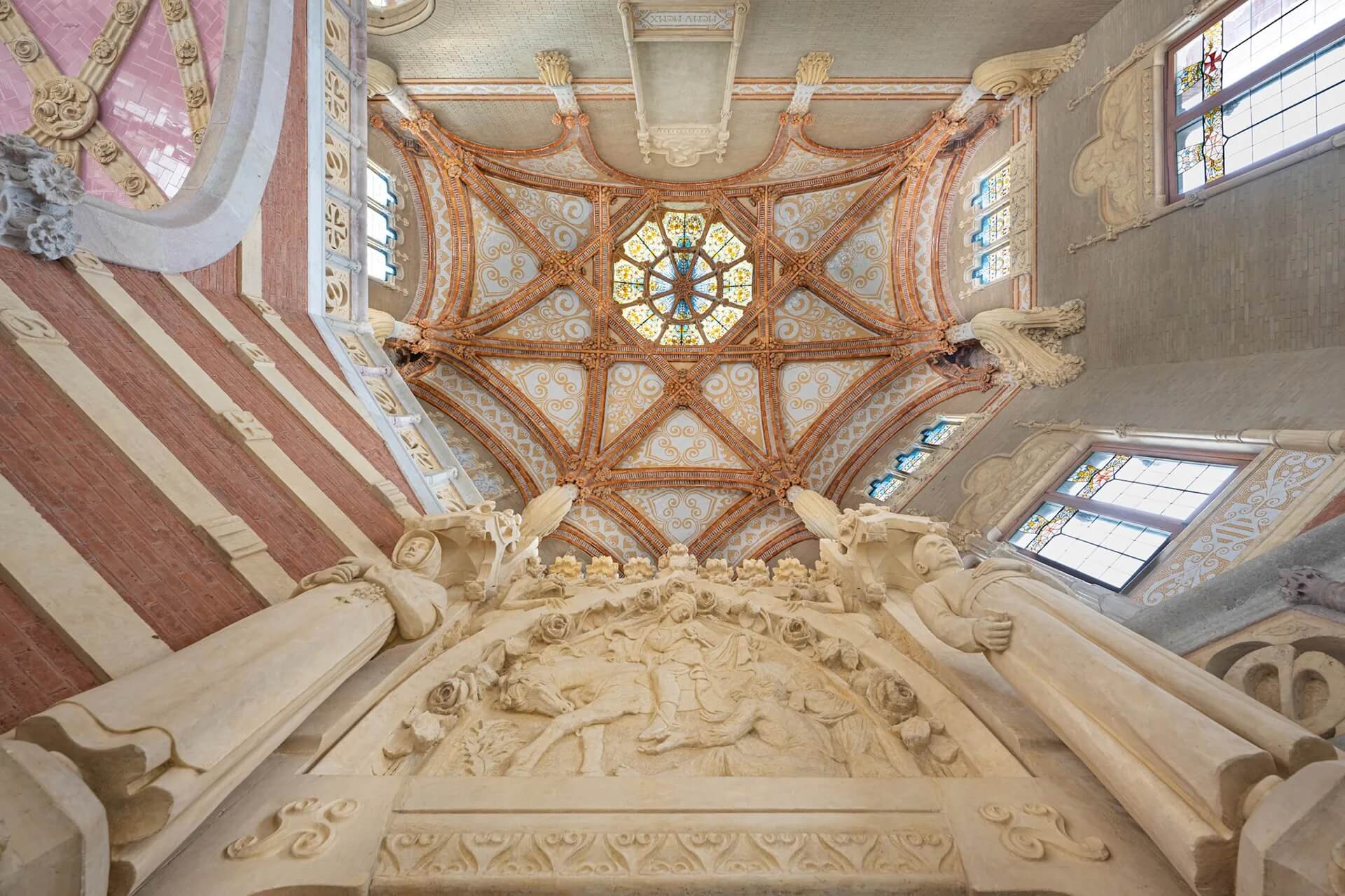 The ceilings within the Hospital de Sant Pau in Barcelona soar high above and are beautifully detailed with carved stone and wood, stained glass windows filtering colored light, and statues of saints who devoted their lives to healing mark the entrance.